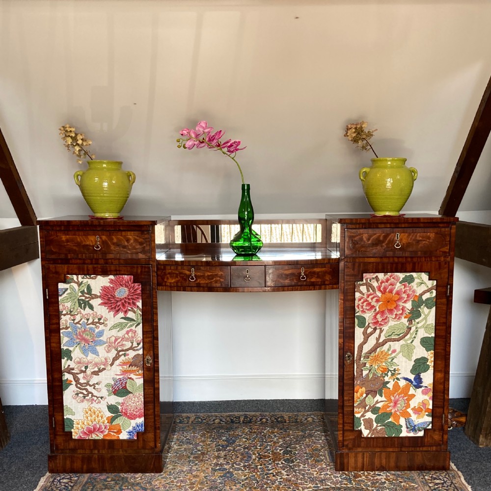 A late Georgian mahogany pedestal sideboard featuring two outer pedestals with floral fabric panels, central drawers, and warm flame mahogany wood grain.