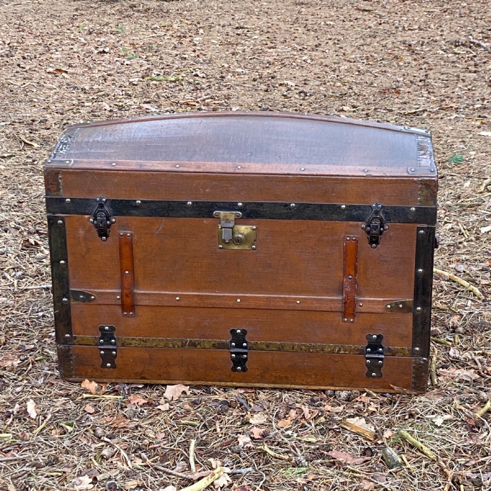 A late nineteenth-century domed steamer trunk with brown fabric covering, dark wooden banding, metal studs, and central brass lock hardware.