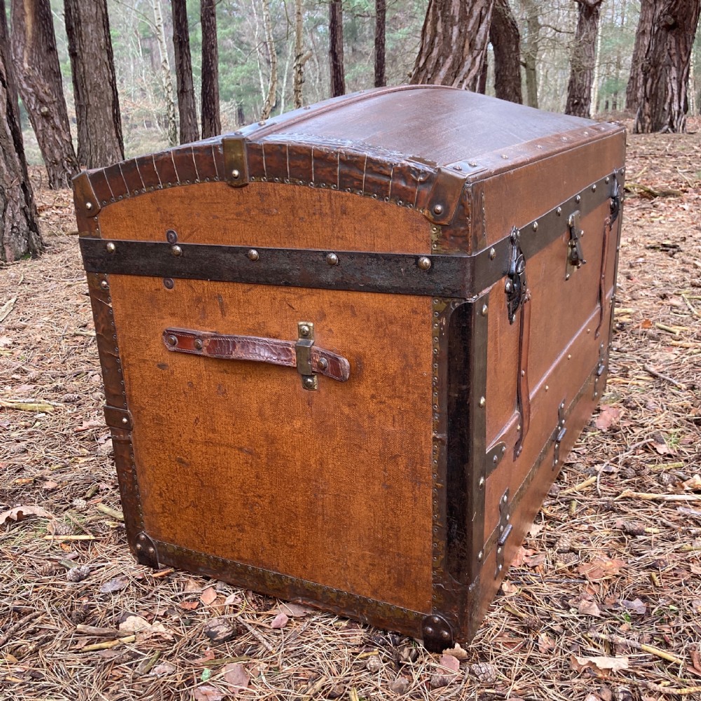 A late nineteenth-century domed steamer trunk with brown fabric covering, dark wooden banding, metal studs, and central brass lock hardware. View II