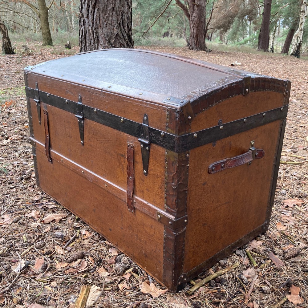 A late nineteenth-century domed steamer trunk with brown fabric covering, dark wooden banding, metal studs, and central brass lock hardware. View XI