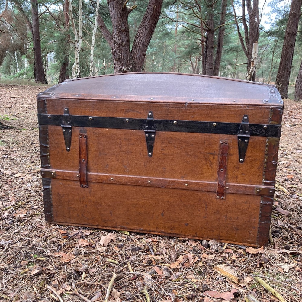 A late nineteenth-century domed steamer trunk with brown fabric covering, dark wooden banding, metal studs, and central brass lock hardware. View XII
