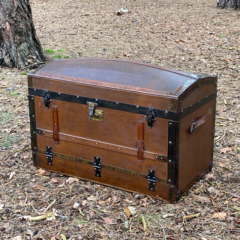A late nineteenth-century domed steamer trunk with brown fabric covering, dark wooden banding, metal studs, and central brass lock hardware. View XIII