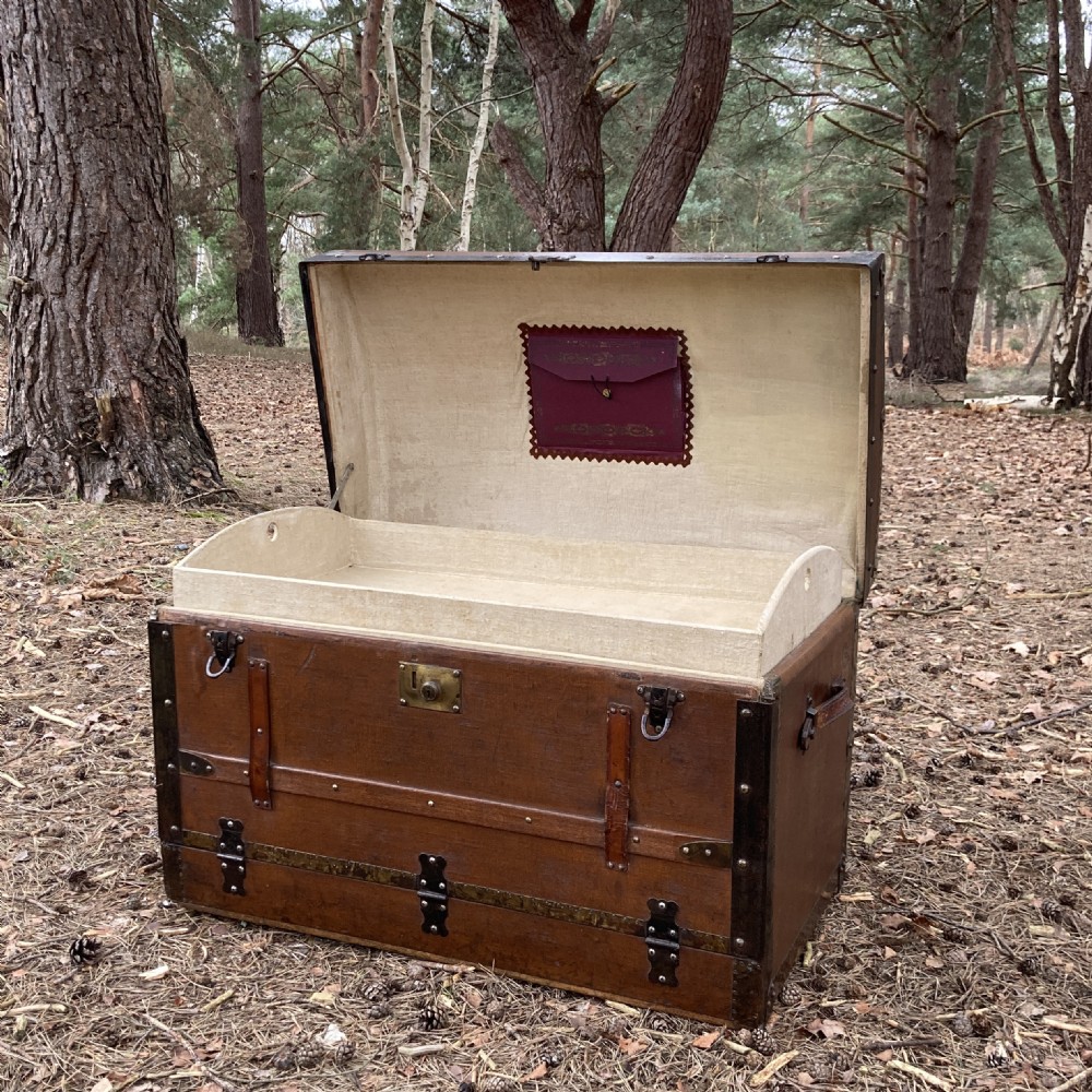 A late nineteenth-century domed steamer trunk with brown fabric covering, dark wooden banding, metal studs, and central brass lock hardware. View XIV