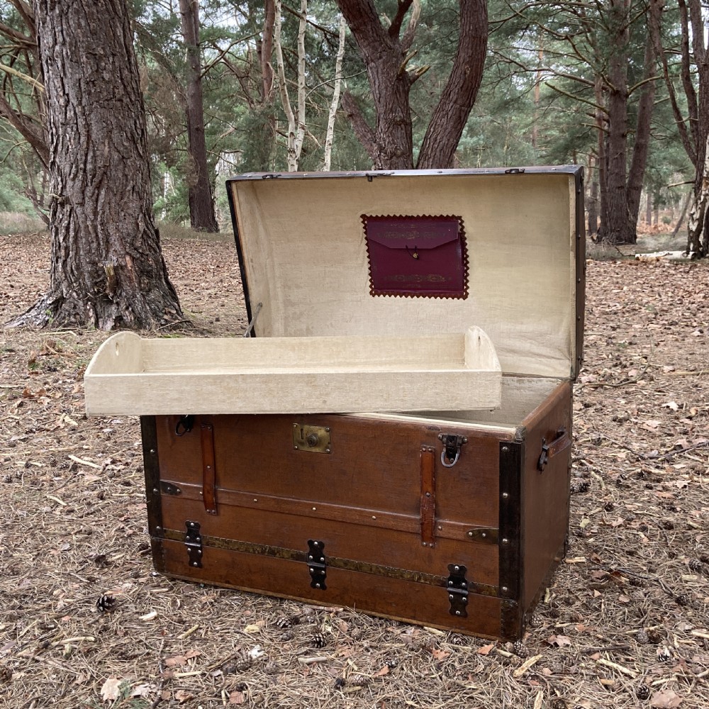 A late nineteenth-century domed steamer trunk with brown fabric covering, dark wooden banding, metal studs, and central brass lock hardware. View XV