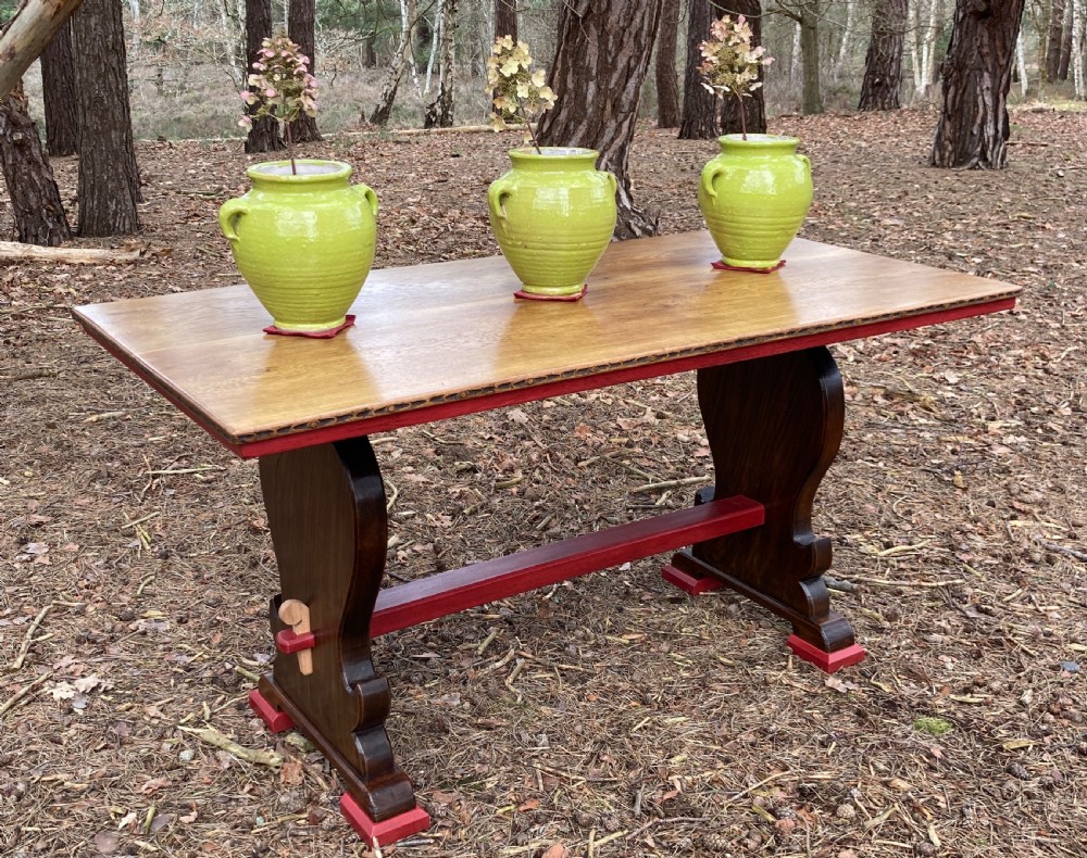 An antique oak and elm refectory table featuring dark trestle leg supports, a red painted stretcher with key joint, and a rectangular timber top.