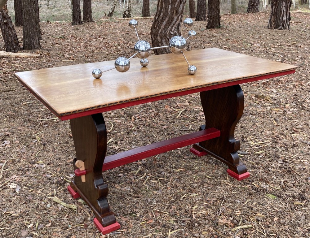 An antique oak and elm refectory table featuring dark trestle leg supports, a red painted stretcher with key joint, and a rectangular timber top. View V