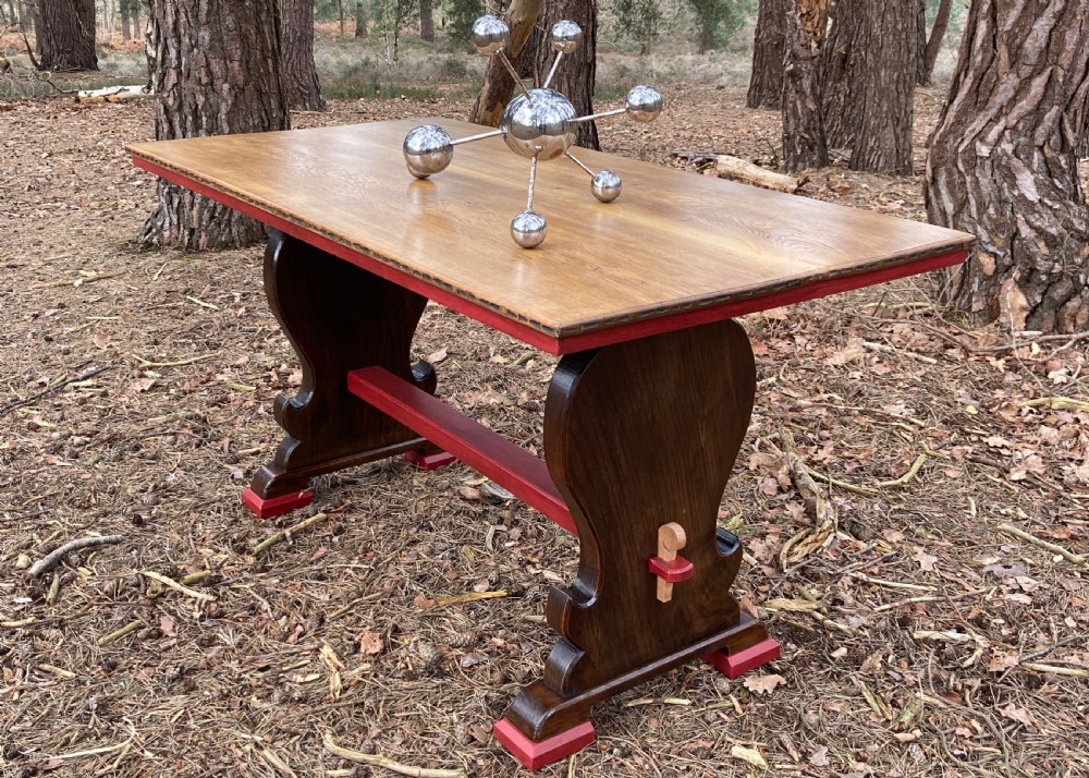 An antique oak and elm refectory table featuring dark trestle leg supports, a red painted stretcher with key joint, and a rectangular timber top. View VI