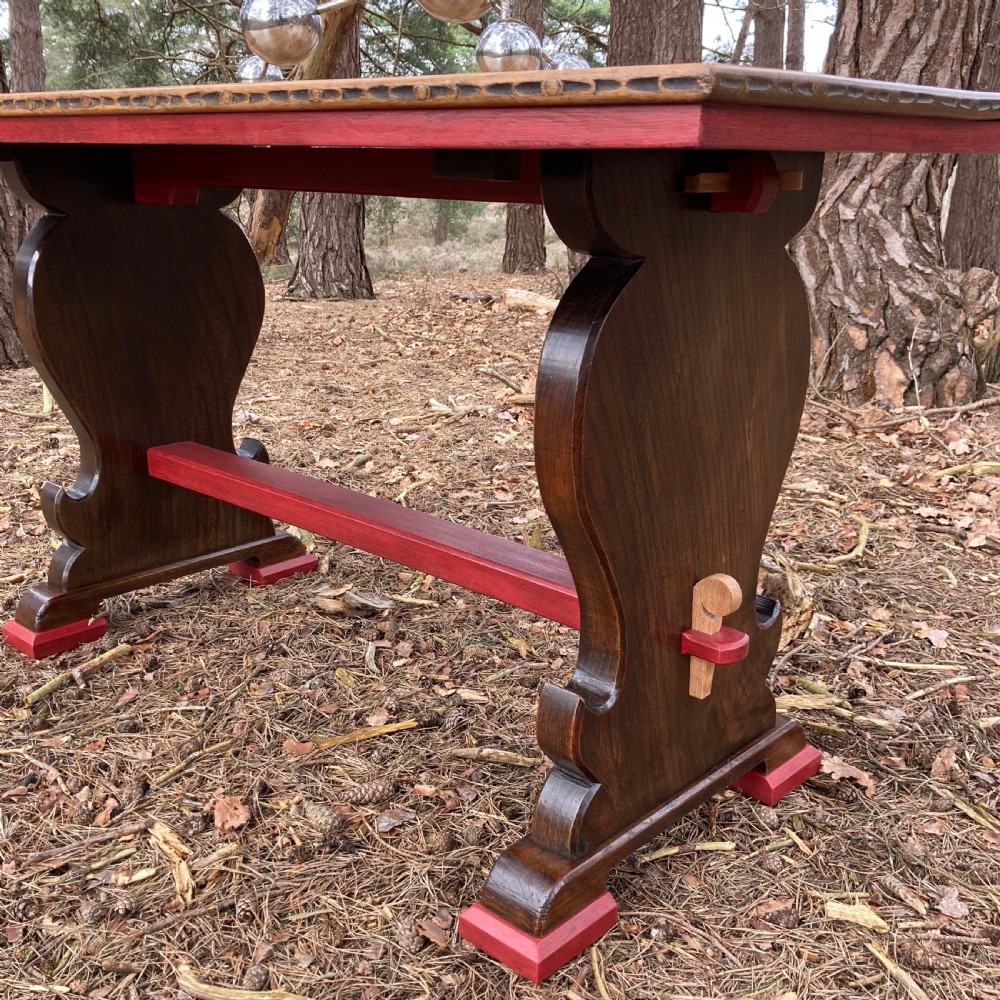 An antique oak and elm refectory table featuring dark trestle leg supports, a red painted stretcher with key joint, and a rectangular timber top. View X