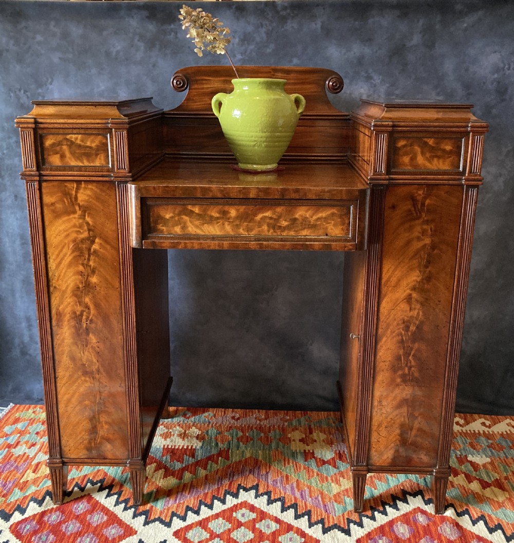 An Early Victorian flame mahogany pedestal sideboard with a central recessed drawer section, scrolled backboard, fluted pilasters, and twin side cupboard doors. View III