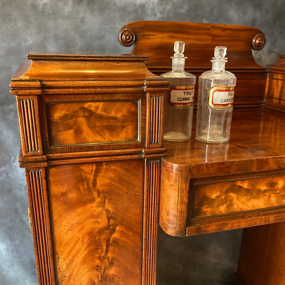 An Early Victorian flame mahogany pedestal sideboard with a central recessed drawer section, scrolled backboard, fluted pilasters, and twin side cupboard doors. View VII