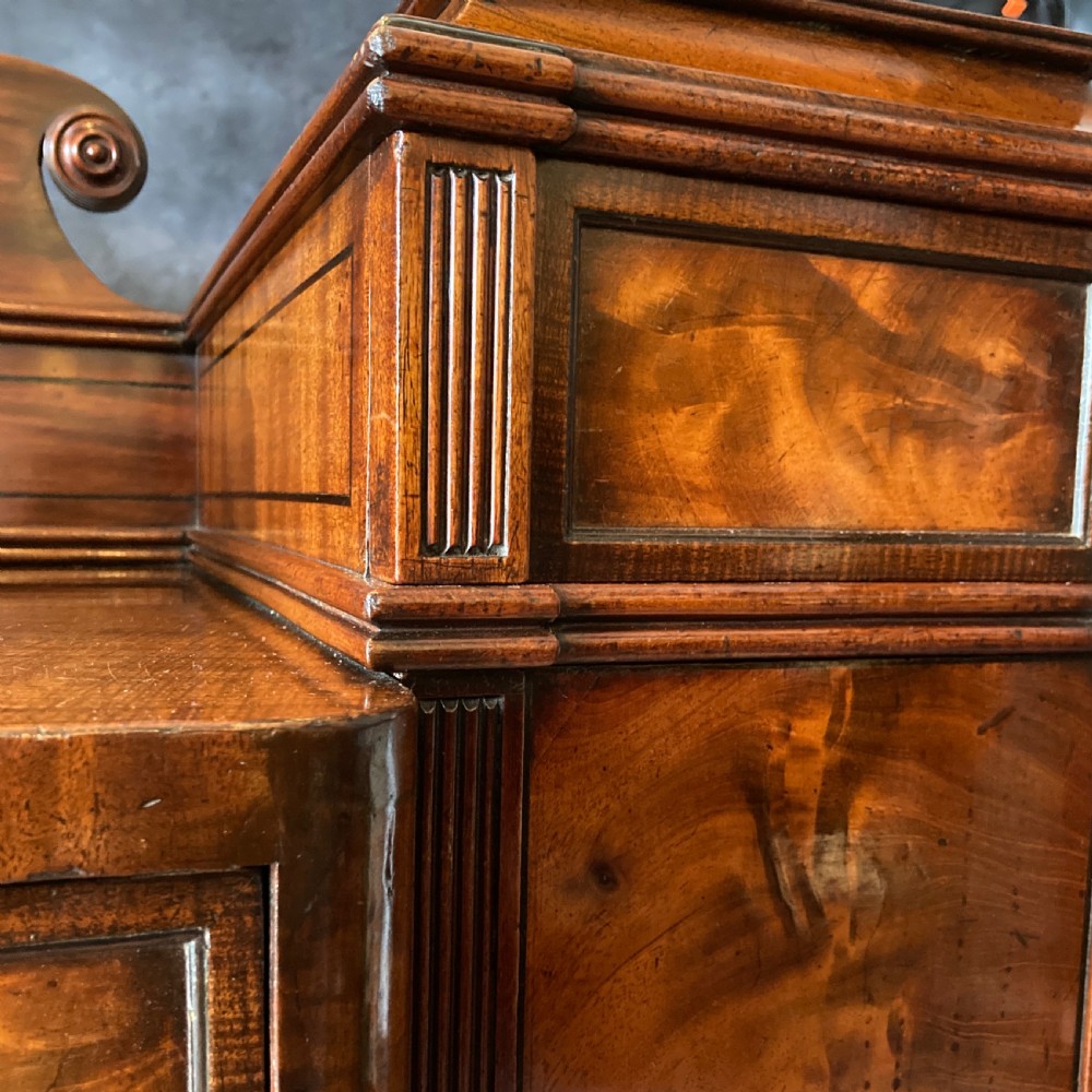 An Early Victorian flame mahogany pedestal sideboard with a central recessed drawer section, scrolled backboard, fluted pilasters, and twin side cupboard doors. View XII
