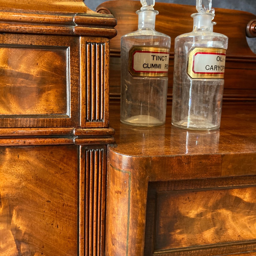 An Early Victorian flame mahogany pedestal sideboard with a central recessed drawer section, scrolled backboard, fluted pilasters, and twin side cupboard doors. View XIII
