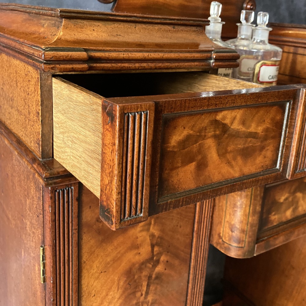 An Early Victorian flame mahogany pedestal sideboard with a central recessed drawer section, scrolled backboard, fluted pilasters, and twin side cupboard doors. View XIV