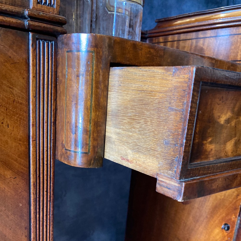 An Early Victorian flame mahogany pedestal sideboard with a central recessed drawer section, scrolled backboard, fluted pilasters, and twin side cupboard doors. View XVI