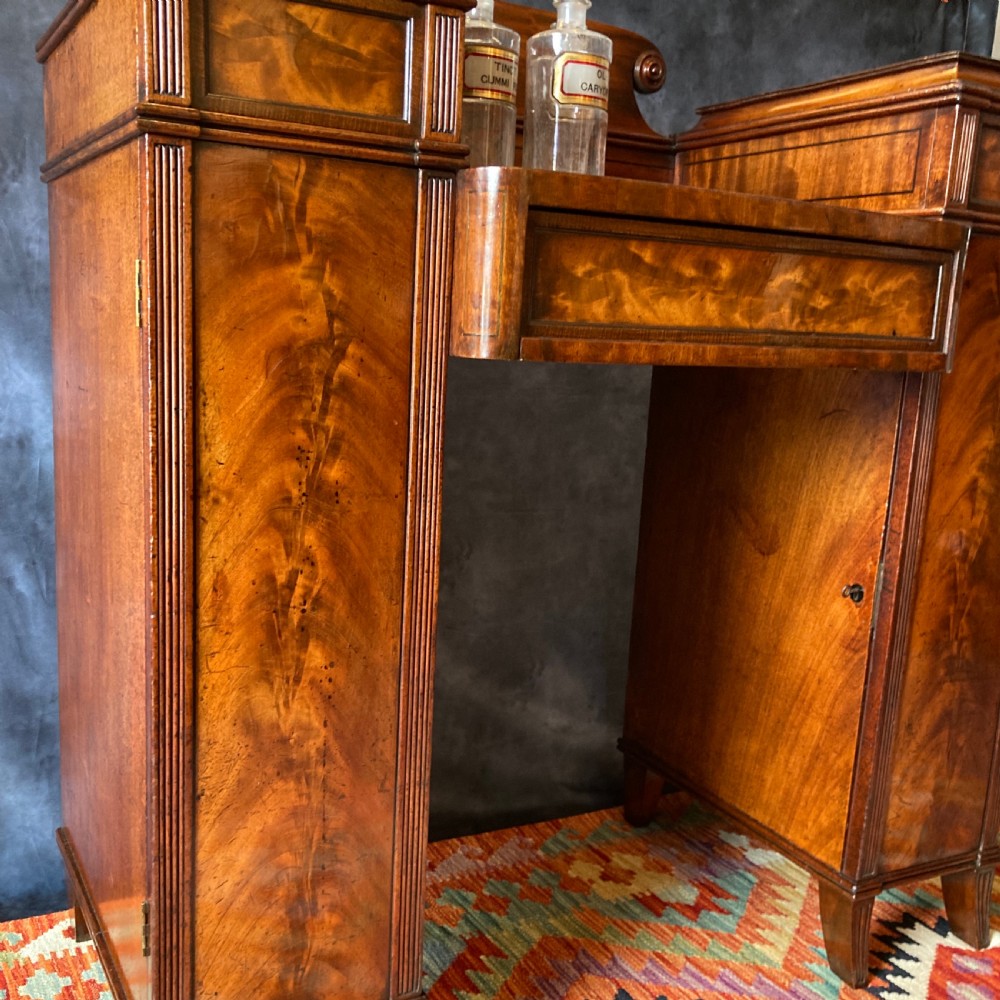 An Early Victorian flame mahogany pedestal sideboard with a central recessed drawer section, scrolled backboard, fluted pilasters, and twin side cupboard doors. View XVII