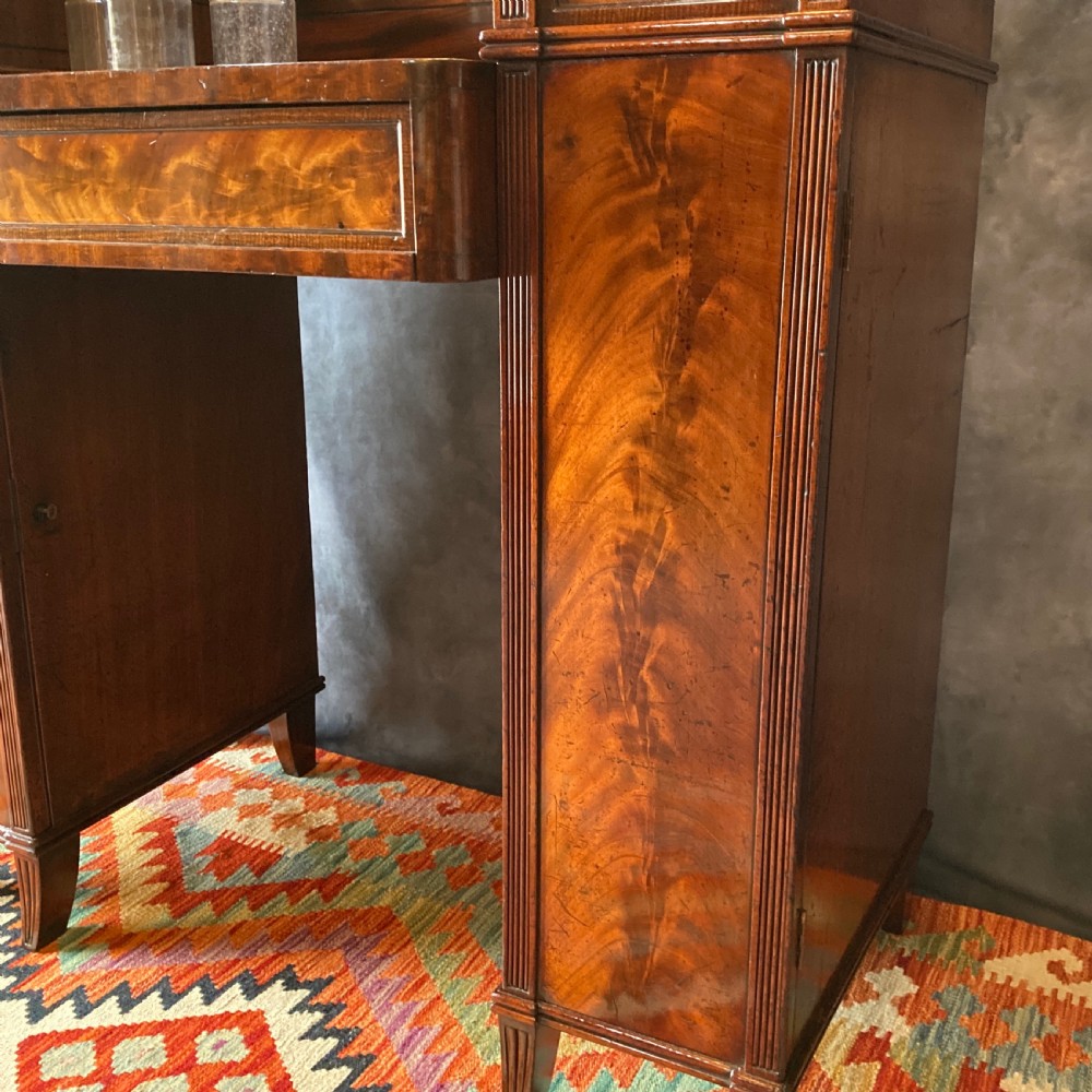 An Early Victorian flame mahogany pedestal sideboard with a central recessed drawer section, scrolled backboard, fluted pilasters, and twin side cupboard doors. View XVIII