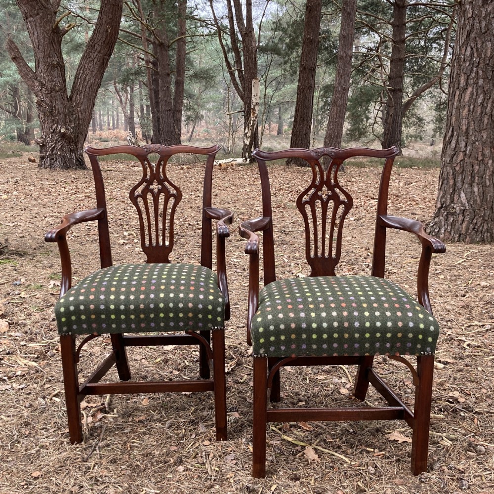 A pair of 1830s mahogany open armchairs featuring carved top rails, pierced splats, swept arms, and seats upholstered in a green patterned fabric.