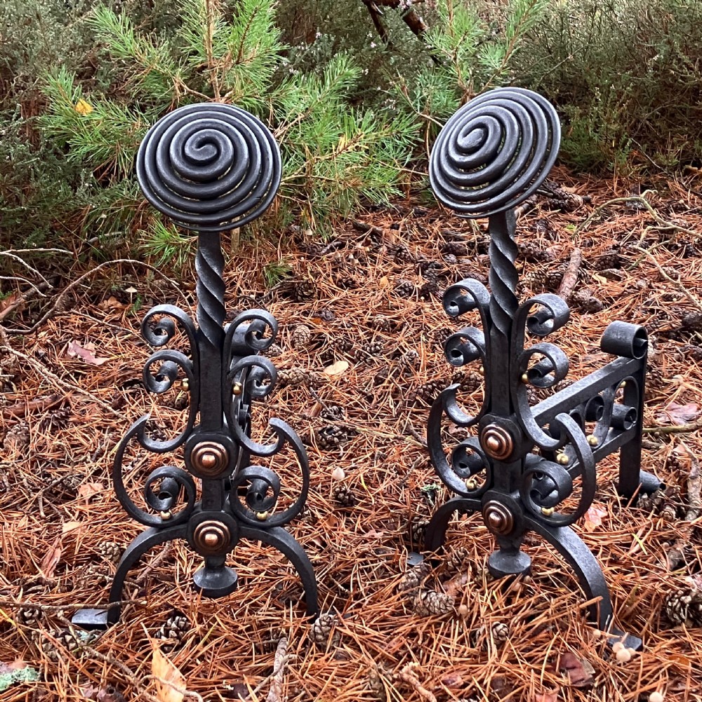 A pair of hand-forged black wrought iron fire dogs featuring spiral terminal tops, twisted stems, scrollwork bases, and copper boss accents.