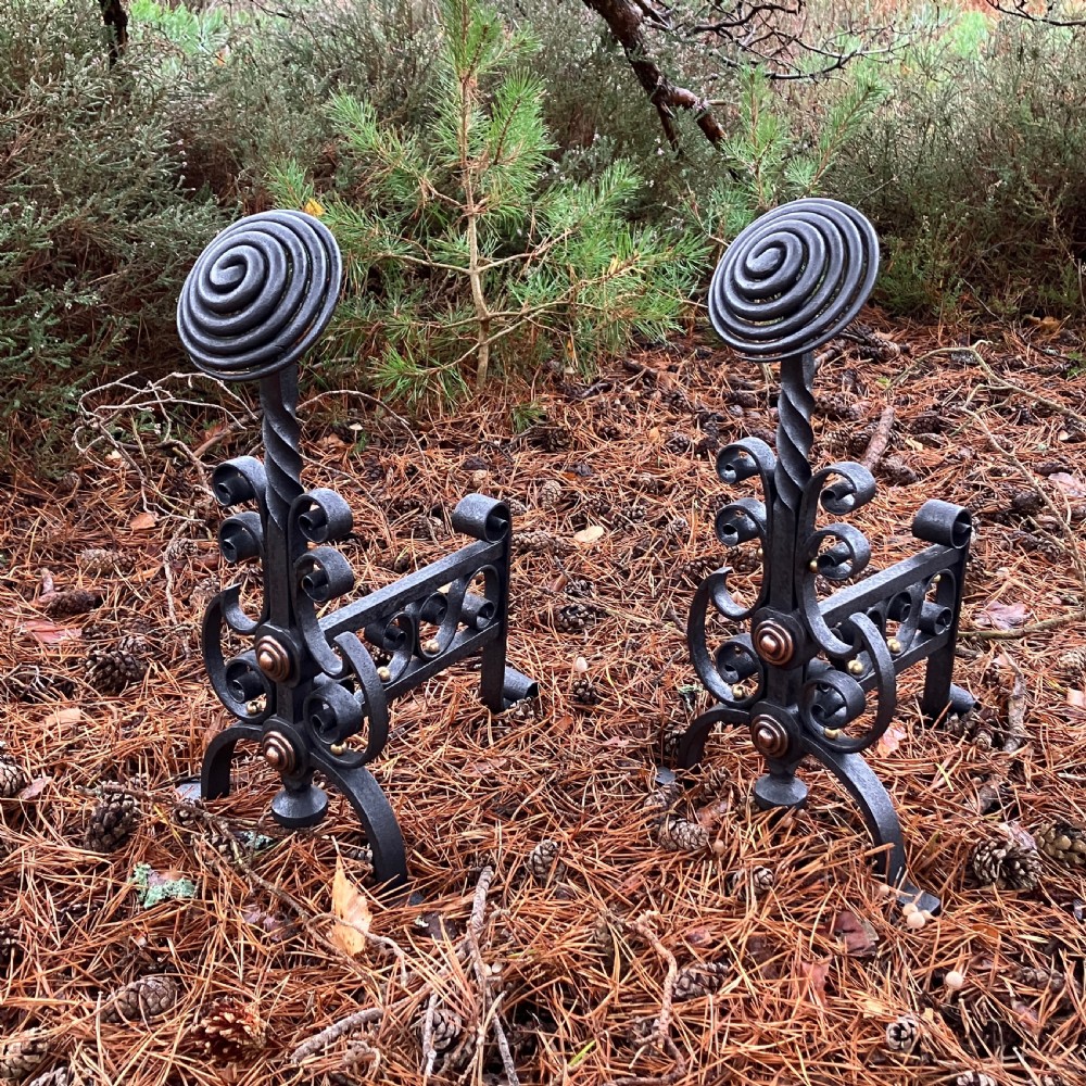A pair of hand-forged black wrought iron fire dogs featuring spiral terminal tops, twisted stems, scrollwork bases, and copper boss accents. View II