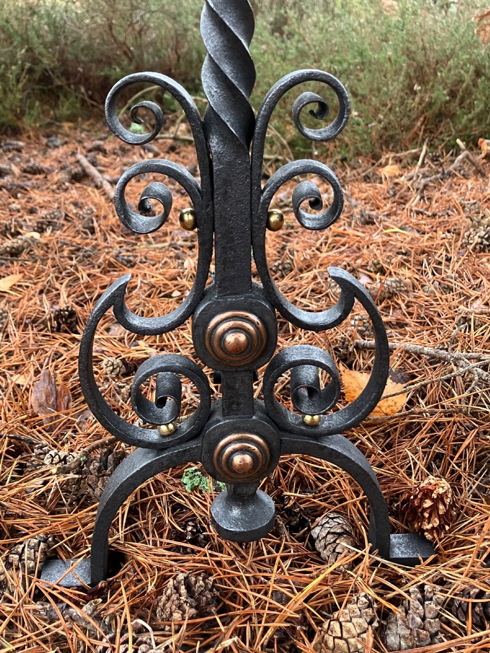 A pair of hand-forged black wrought iron fire dogs featuring spiral terminal tops, twisted stems, scrollwork bases, and copper boss accents. View VII
