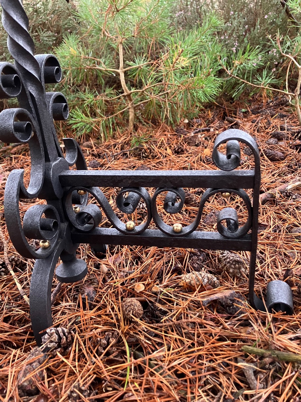 A pair of hand-forged black wrought iron fire dogs featuring spiral terminal tops, twisted stems, scrollwork bases, and copper boss accents. View IX
