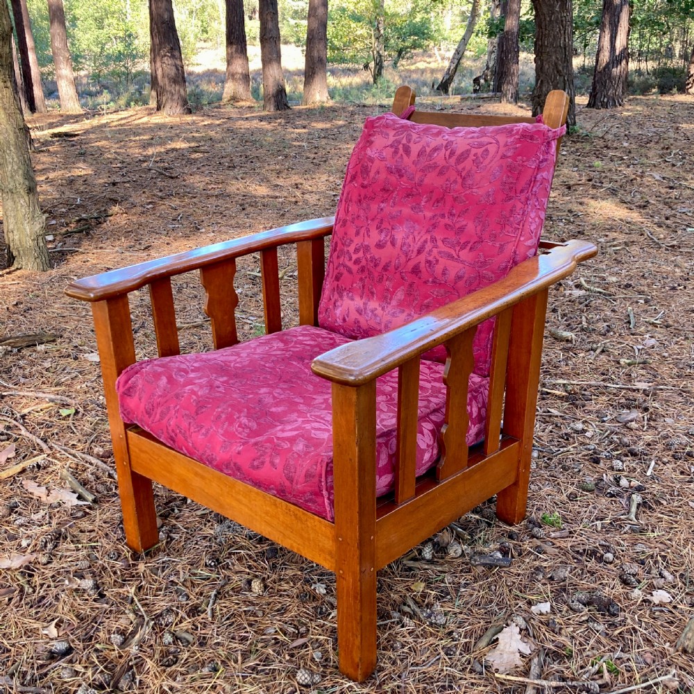 An Edwardian teak reclining armchair featuring slatted side panels, wide flat armrests, and pink floral upholstered cushions.
