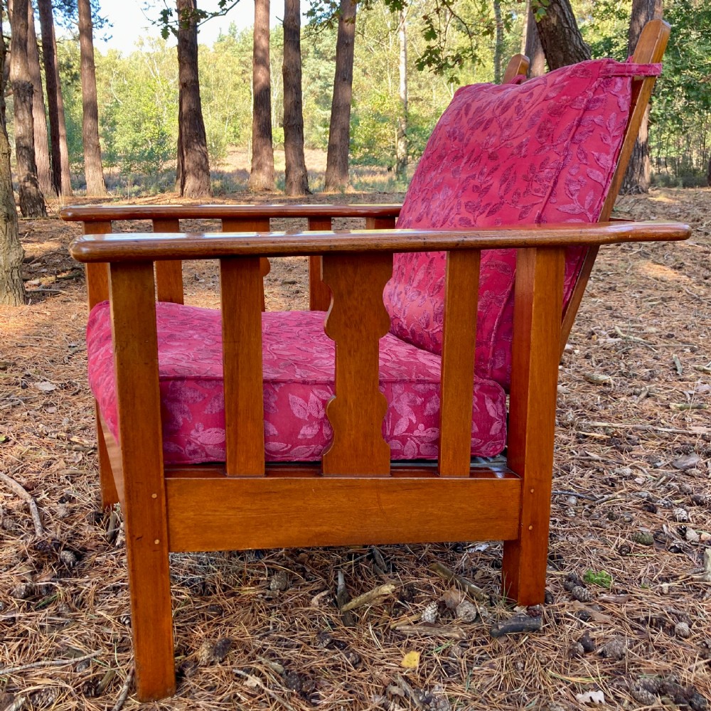 An Edwardian teak reclining armchair featuring slatted side panels, wide flat armrests, and pink floral upholstered cushions. View V