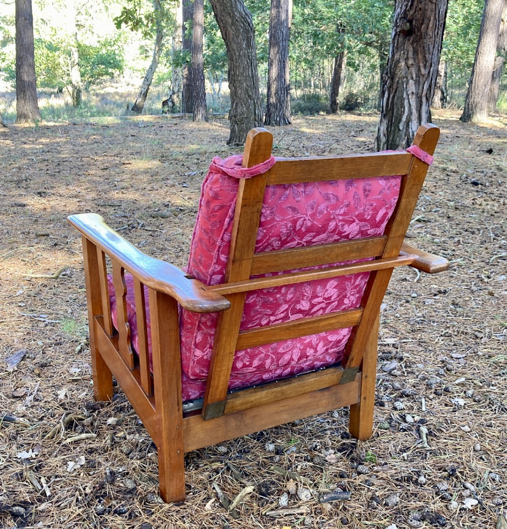 An Edwardian teak reclining armchair featuring slatted side panels, wide flat armrests, and pink floral upholstered cushions. View VI
