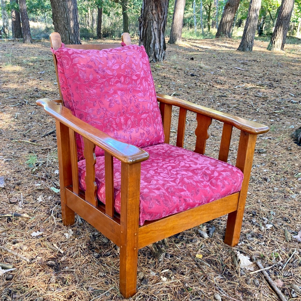 An Edwardian teak reclining armchair featuring slatted side panels, wide flat armrests, and pink floral upholstered cushions. View VII