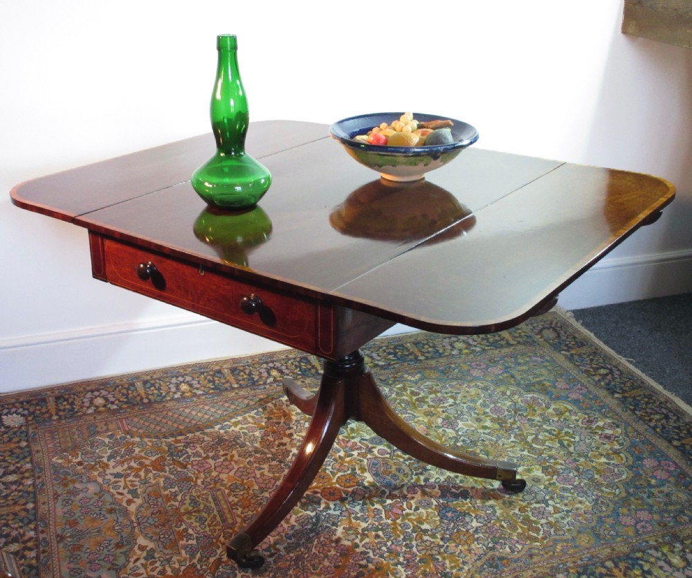A Georgian mahogany Pembroke table featuring two hinged drop leaves, a single frieze drawer, and a central turned pedestal on four splayed legs with brass castors.