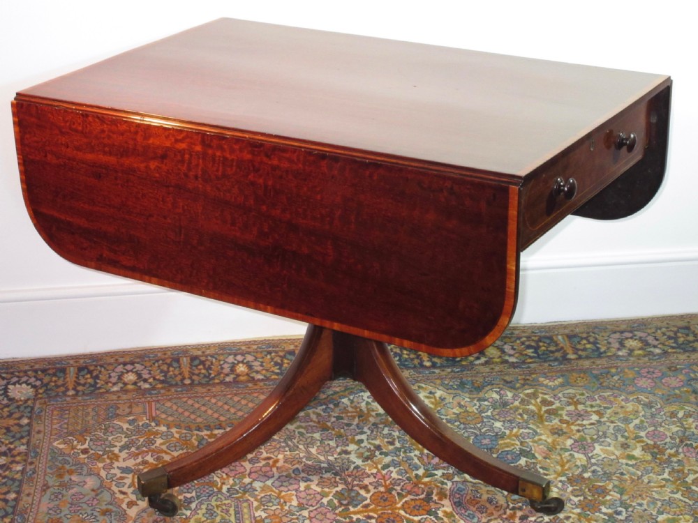 A Georgian mahogany Pembroke table featuring two hinged drop leaves, a single frieze drawer, and a central turned pedestal on four splayed legs with brass castors. View III