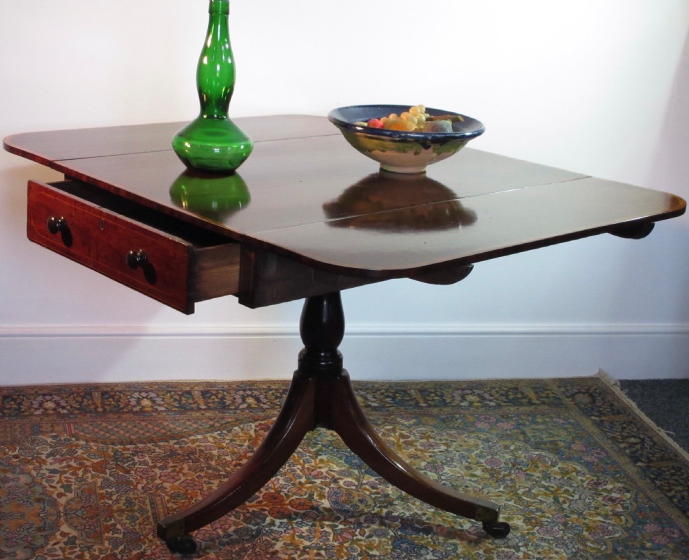 A Georgian mahogany Pembroke table featuring two hinged drop leaves, a single frieze drawer, and a central turned pedestal on four splayed legs with brass castors. View VI