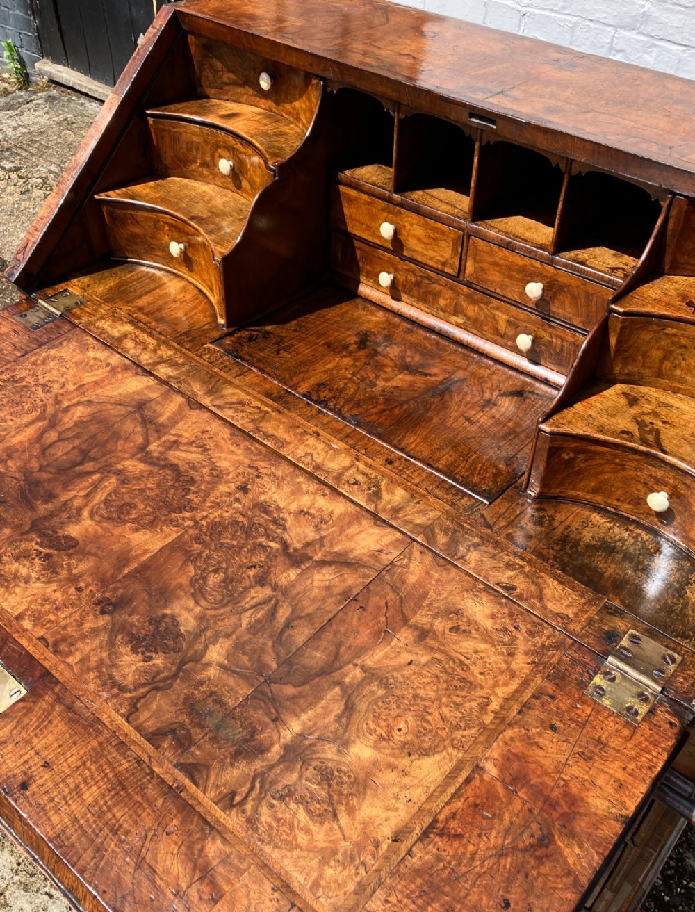 An early eighteenth-century English walnut fall-front bureau featuring burr veneer panels, decorative brass escutcheons and handles, and turned bun feet. View VI