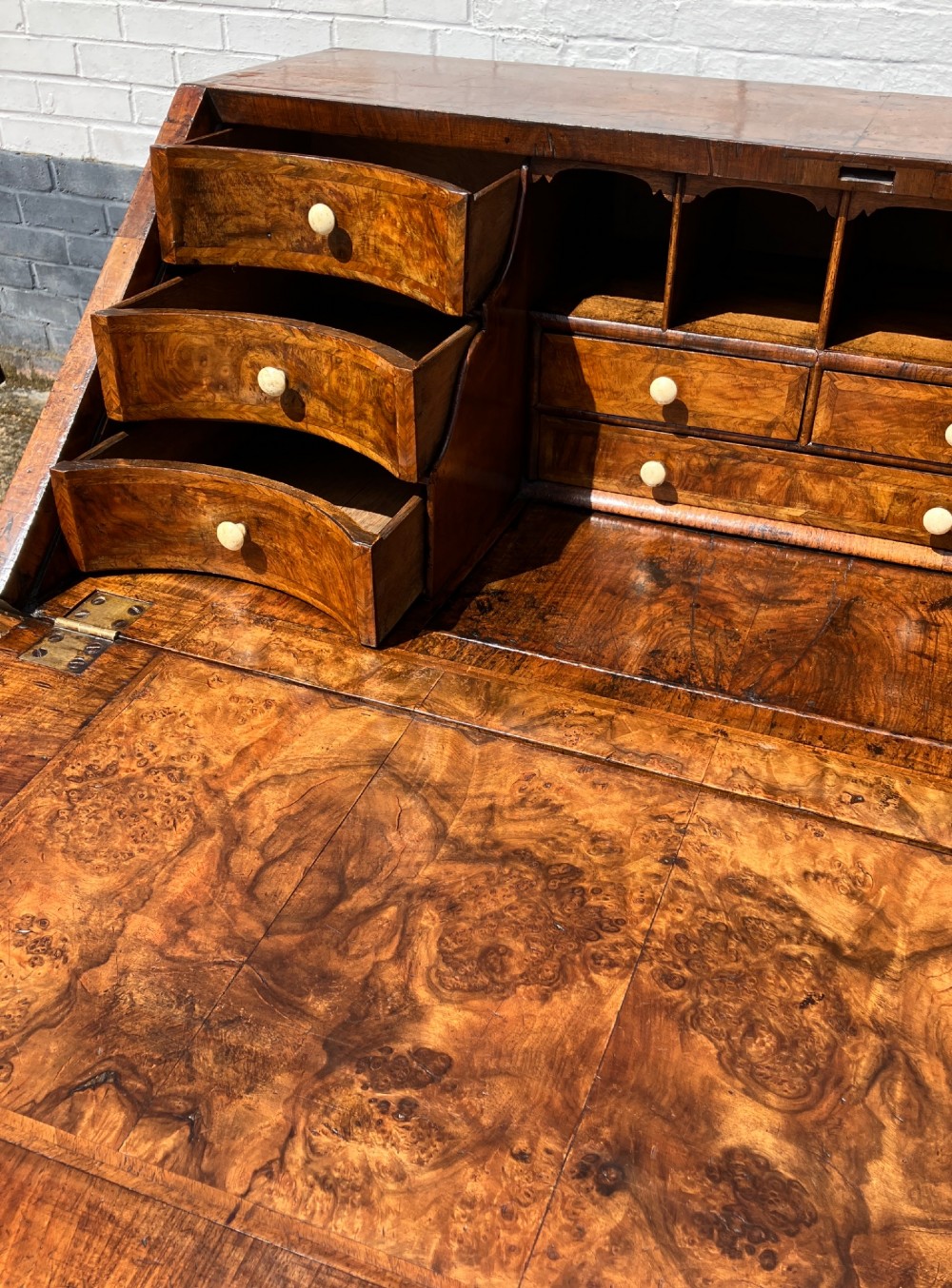 An early eighteenth-century English walnut fall-front bureau featuring burr veneer panels, decorative brass escutcheons and handles, and turned bun feet. View VII