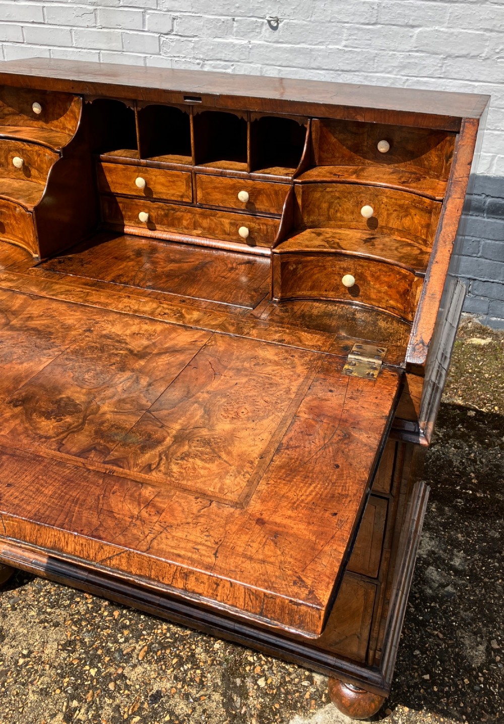 An early eighteenth-century English walnut fall-front bureau featuring burr veneer panels, decorative brass escutcheons and handles, and turned bun feet. View VIII