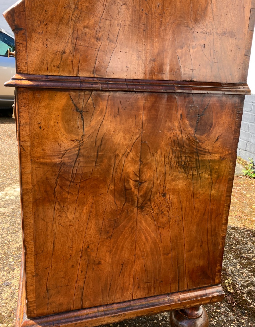 An early eighteenth-century English walnut fall-front bureau featuring burr veneer panels, decorative brass escutcheons and handles, and turned bun feet. View IX