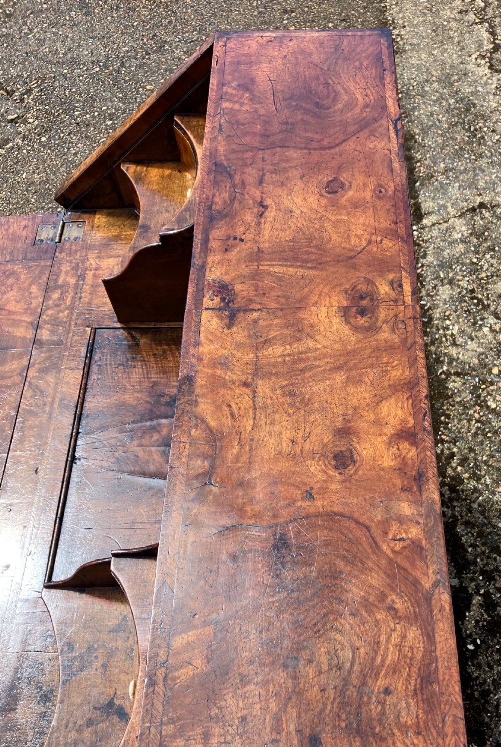 An early eighteenth-century English walnut fall-front bureau featuring burr veneer panels, decorative brass escutcheons and handles, and turned bun feet. View XI