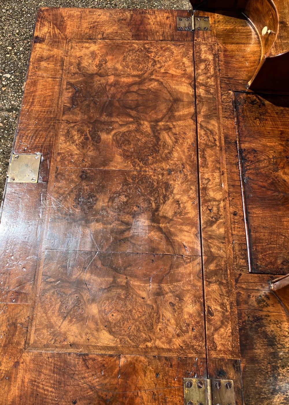 An early eighteenth-century English walnut fall-front bureau featuring burr veneer panels, decorative brass escutcheons and handles, and turned bun feet. View XII