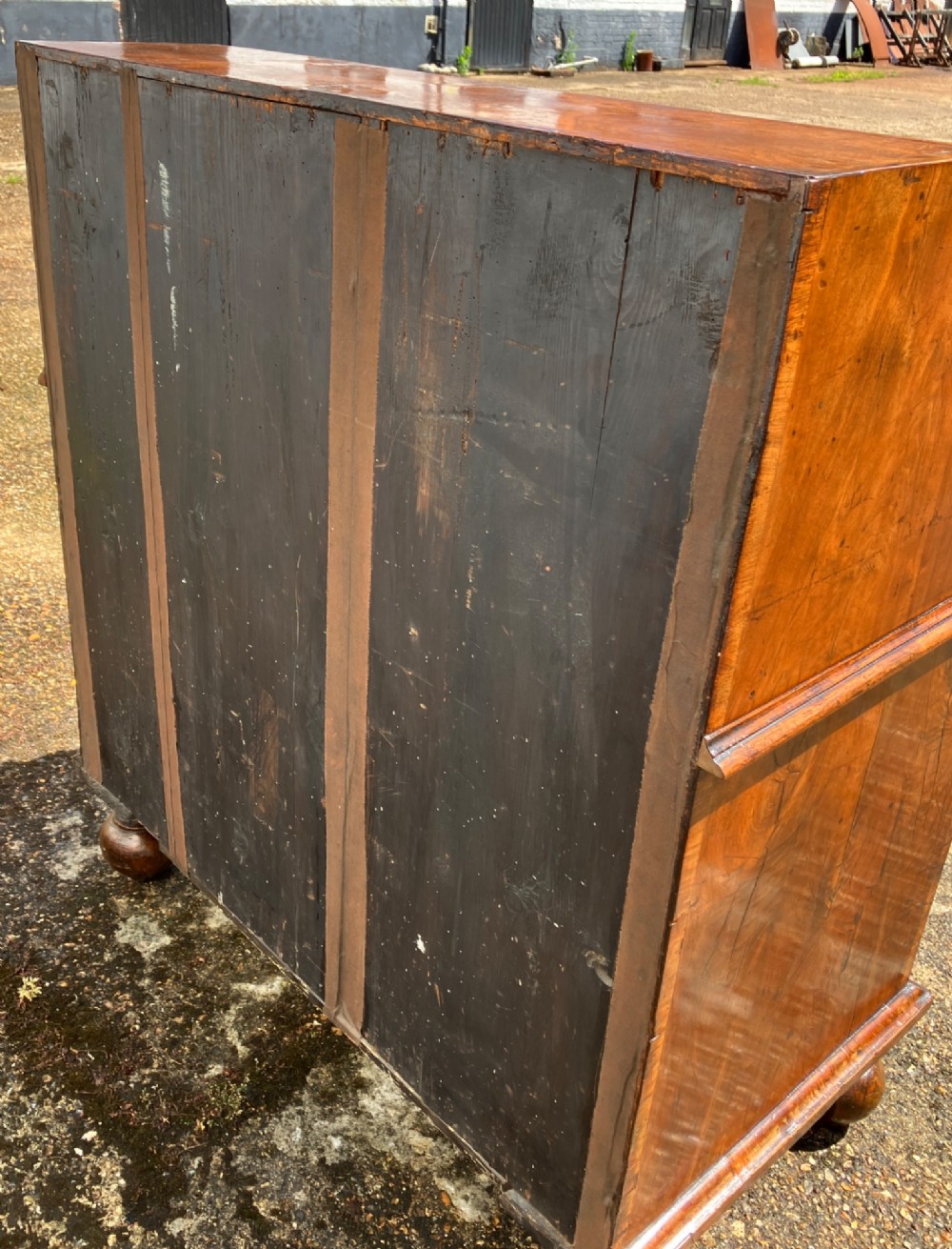 An early eighteenth-century English walnut fall-front bureau featuring burr veneer panels, decorative brass escutcheons and handles, and turned bun feet. View XIV