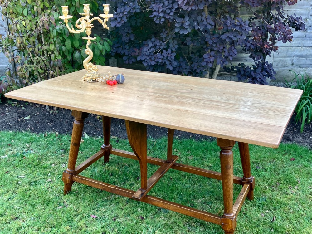 A solid medium oak Arts and Crafts refectory dining table with drop-leaf sides, turned angled legs, and a low stretcher base. View II