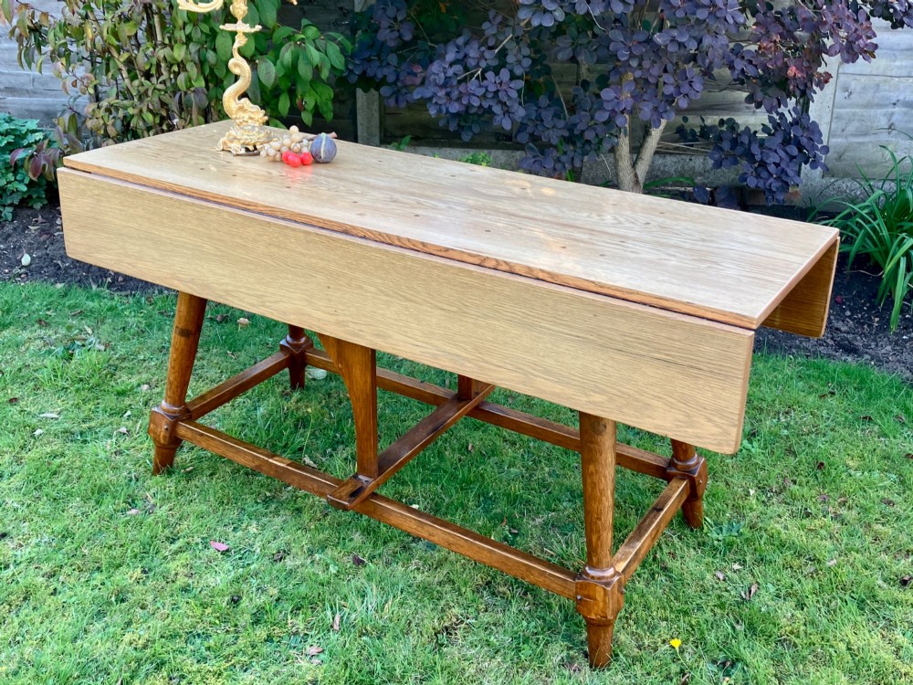 A solid medium oak Arts and Crafts refectory dining table with drop-leaf sides, turned angled legs, and a low stretcher base. View III