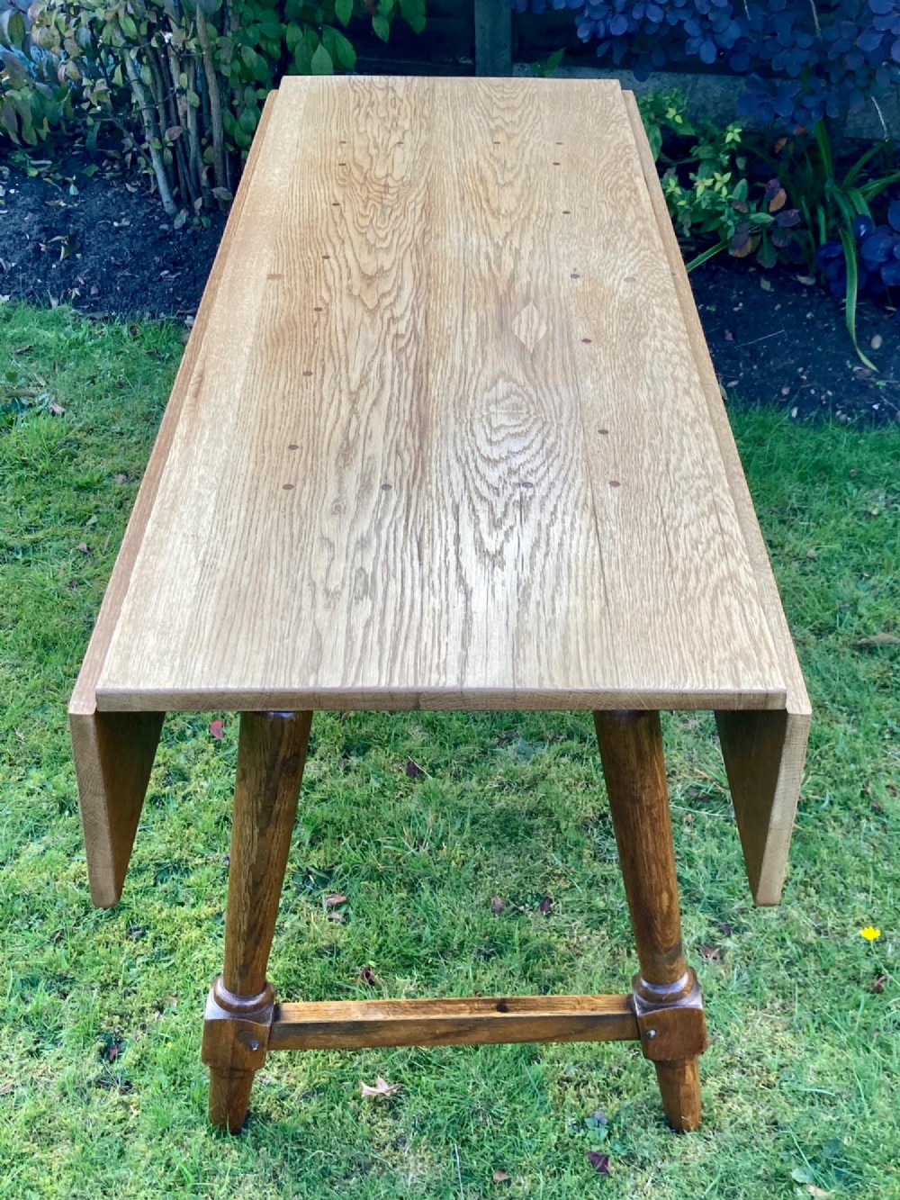 A solid medium oak Arts and Crafts refectory dining table with drop-leaf sides, turned angled legs, and a low stretcher base. View IV