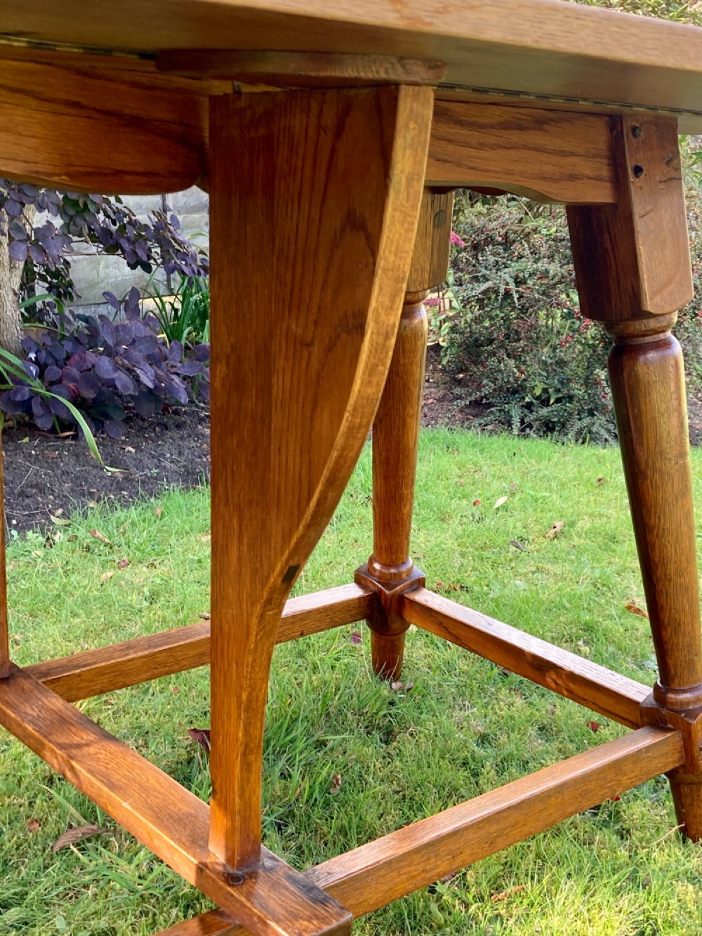 A solid medium oak Arts and Crafts refectory dining table with drop-leaf sides, turned angled legs, and a low stretcher base. View VII