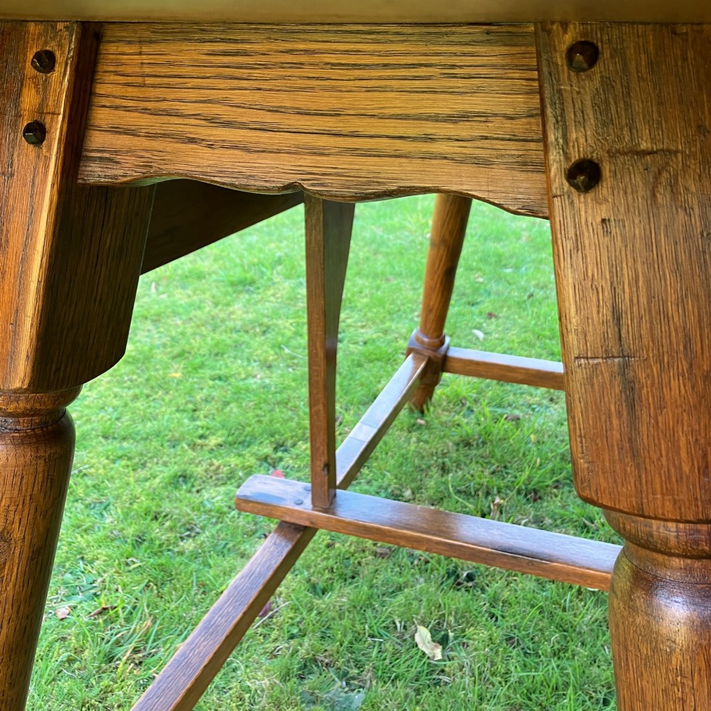 A solid medium oak Arts and Crafts refectory dining table with drop-leaf sides, turned angled legs, and a low stretcher base. View X