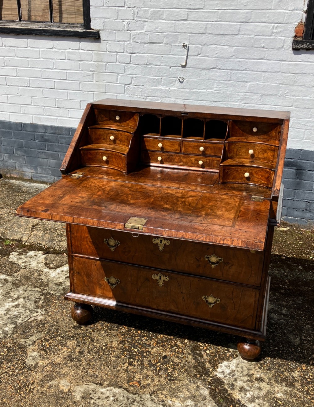 An early 18th-century English walnut fall front bureau featuring figured timber veneers, brass handles, and turned bun feet. View IV