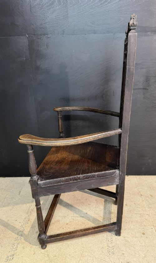 An antique dark oak open armchair featuring a tall carved back panel decorated with Gothic tracery motifs, curved armrests, and turned front legs. View VI
