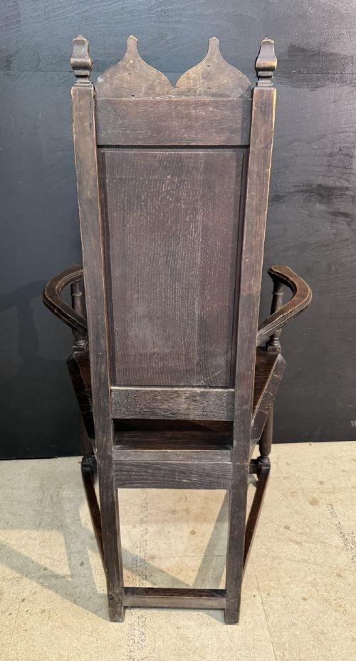 An antique dark oak open armchair featuring a tall carved back panel decorated with Gothic tracery motifs, curved armrests, and turned front legs. View VII