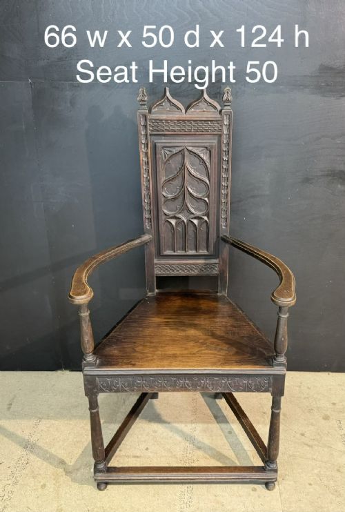 An antique dark oak open armchair featuring a tall carved back panel decorated with Gothic tracery motifs, curved armrests, and turned front legs. View VIII