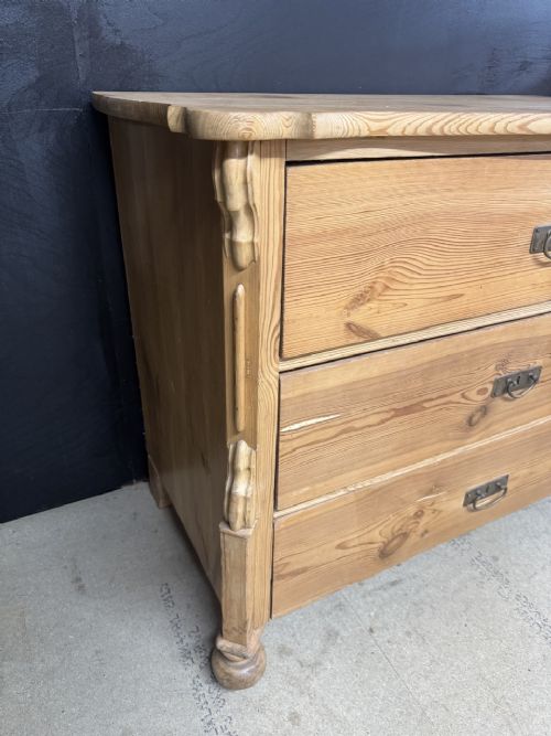 A three-drawer stripped pine chest of drawers featuring carved side corbels, brass drop handles, and turned bun feet. View V