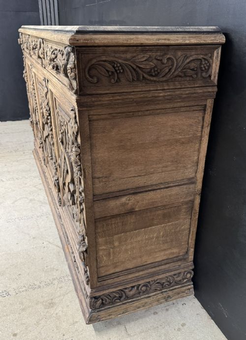 A three-door carved light oak sideboard featuring detailed relief panels depicting artistic and musical instruments. View XIV